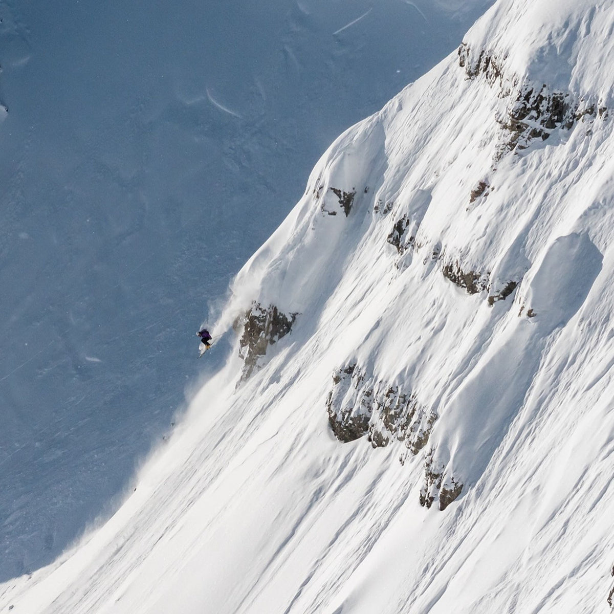 Skier wearing the Thurston Wind Pro® Alpine Hat in glacier grey/black, tuning skis outdoors in falling snow